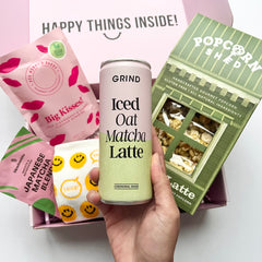 Hand holding a can of 'Grind Iced Oat Matcha Latte' with various food products in the background.