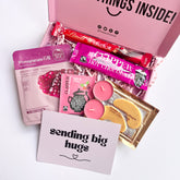 Pink gift box with herbal tea, hot chocolate, scented tealights, gourmet chocolate bar and a card reading 'sending big hugs'.