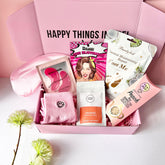 A pink Jumbo Pamper Box open to display its contents, which include a pair of pink smiley socks, a coffee scrub pouch, a satin sleep mask, a Korean face mask sheet, a coconut foot pack, a herbal tea pop and pink eye patches. All arranged neatly inside the box.