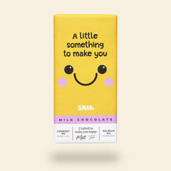 A yellow chocolate bar packaging with a smiling face and the text 'A little something to make you' on top. The brand 'GNAW' is visible at the bottom with the product description 'Milk Chocolate' and additional text indicating compostable packaging.