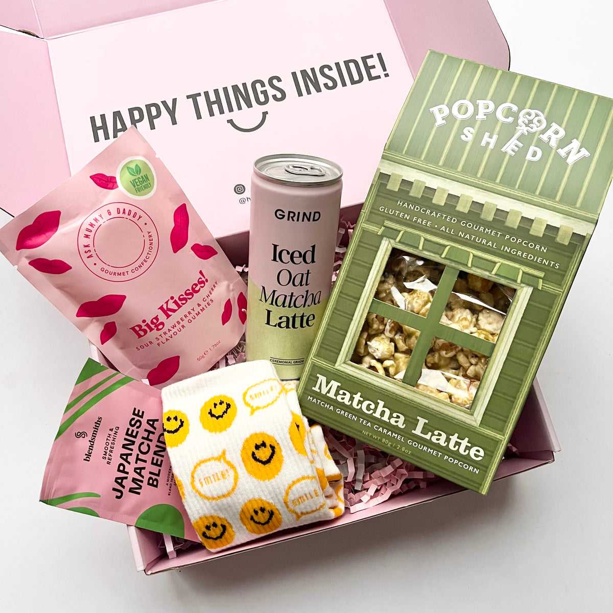 Assorted snacks including a sweets bag, Iced Oat Matcha latte can and green Popcorn box on a white background