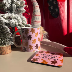 Mug with gingerbread design and matching coaster on a table with Christmas decorations.