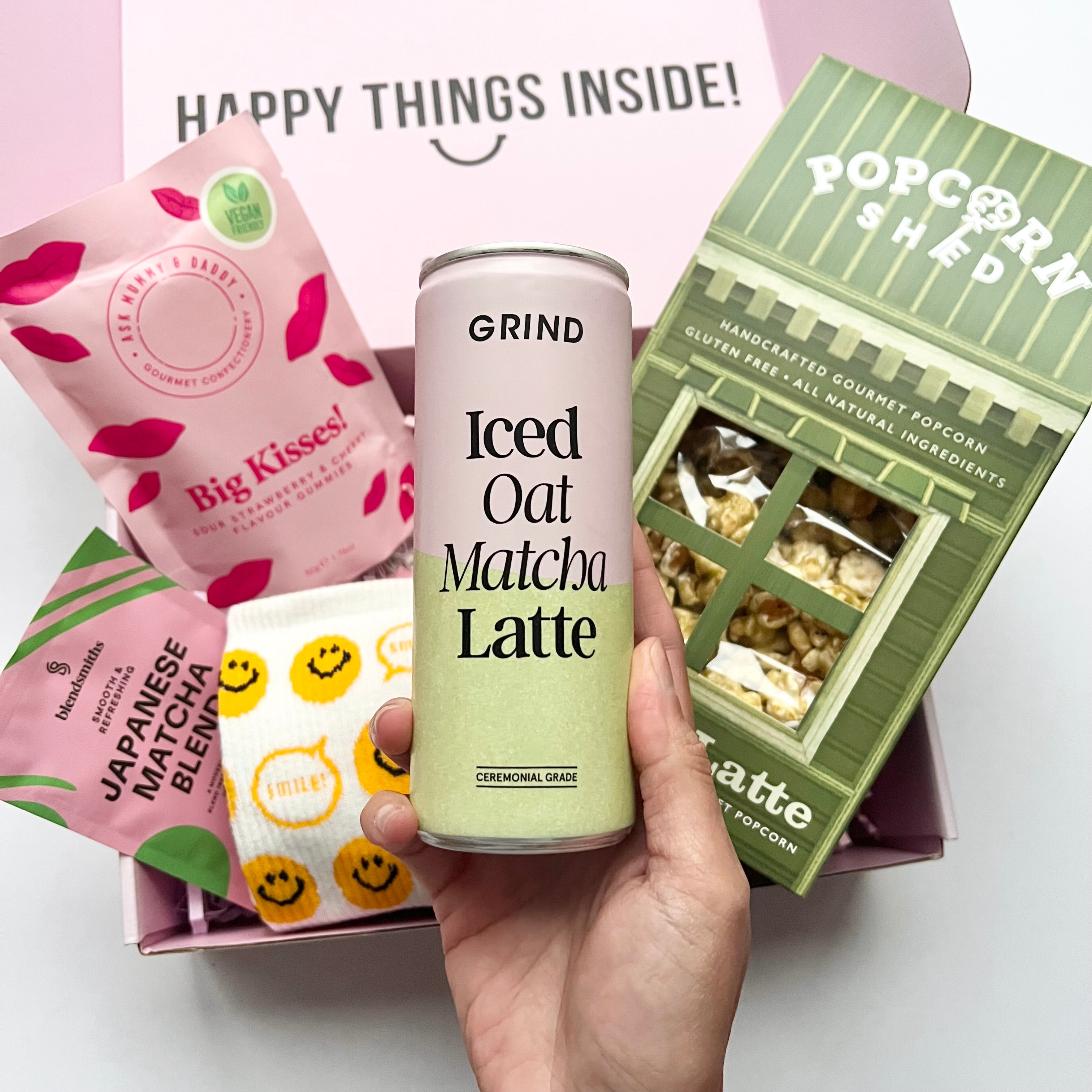 Hand holding a can of 'Grind Iced Oat Matcha Latte' with various food products in the background.