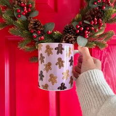 Hand holding a mug with gingerbread man pattern in front of a red door with Christmas decorations.